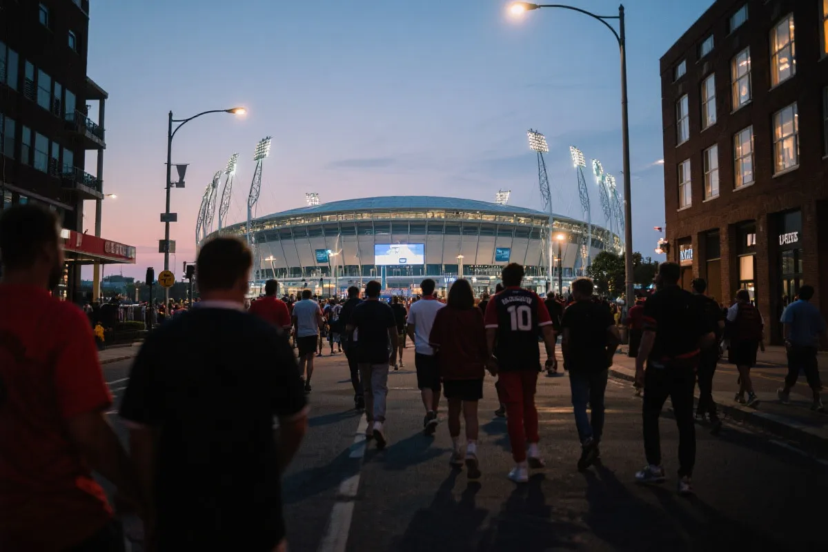 球迷在傍晚沿着步行通道前往球场，城市灯光与赛前氛围